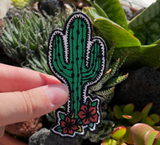 Kaktus Blumen Patch gehalten von einer Hand mit Kakteen im Hintergrund