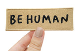 Frauenhand hält ockerfarbenen Be Human Patch