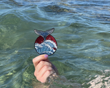 Wal Patch mit dem Meer im Hintergrund gehalten von einer Frauenhand