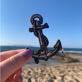 Frauenhand hält den Anker Patch im Urlaub mit Strand im Hintergrund
