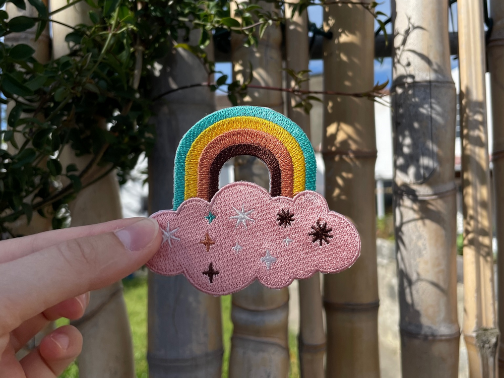 Regenbogen Patch gehalten von einer Frauenhand mit Bambuszaun im Hintergund