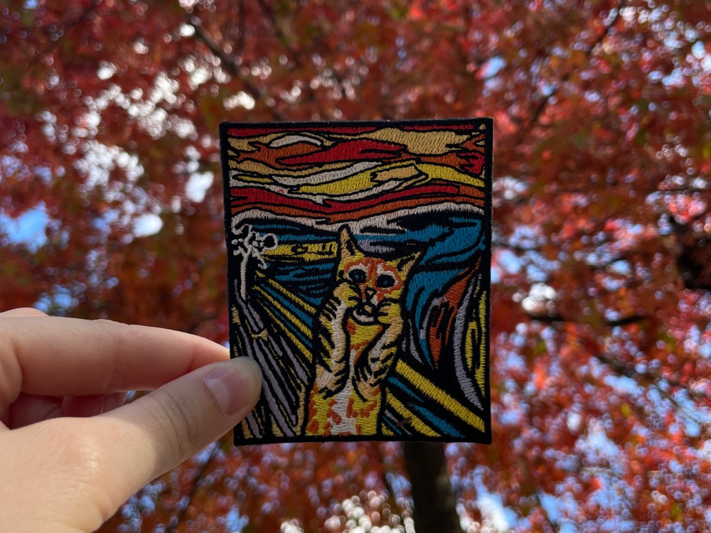Katzen Patch gehalten von einer Frauenhand mit Herbstbaum im Hintergrund