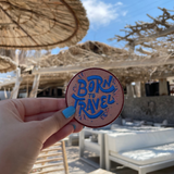 Born to Travel Patch gehalten von einer Frauenhand mit einer Strandbar im Hintergrund