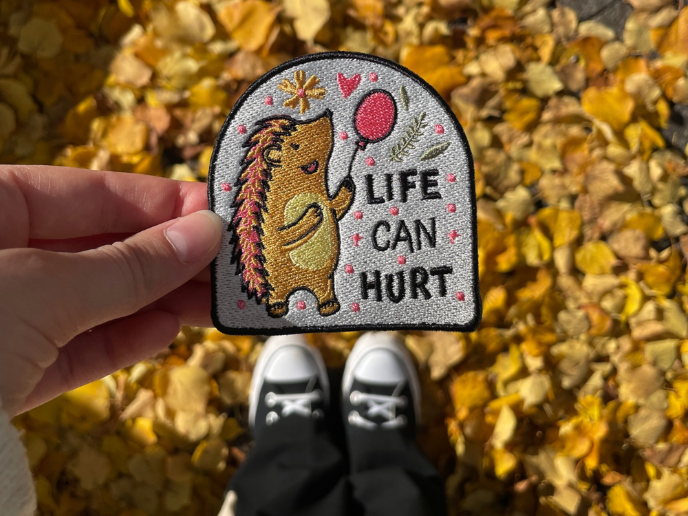 Frauenhand hält den Igel Patch mit herbstlichen Hintergrund