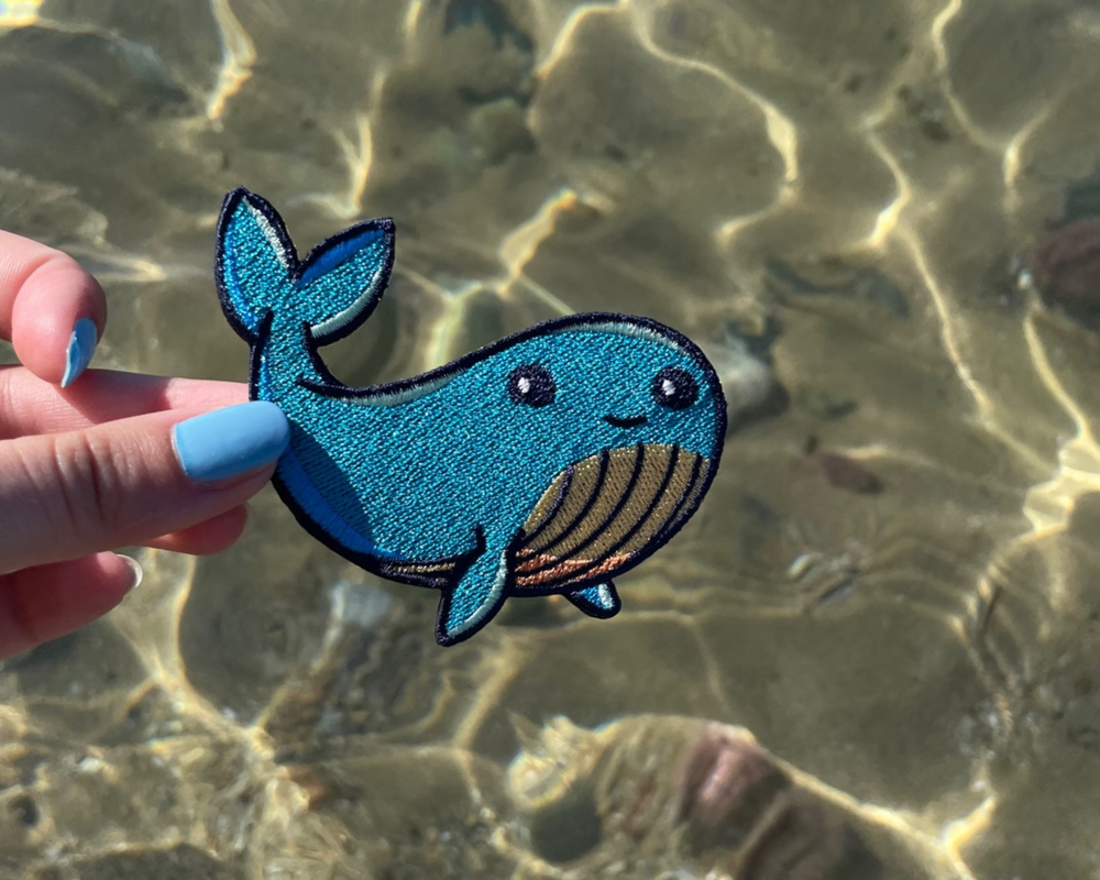 Wal Patch gehalten von einer Frauenhand mit dem Meer im Hintergrund