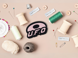 UFO Patch mit Nähzeug im Hintergrund
