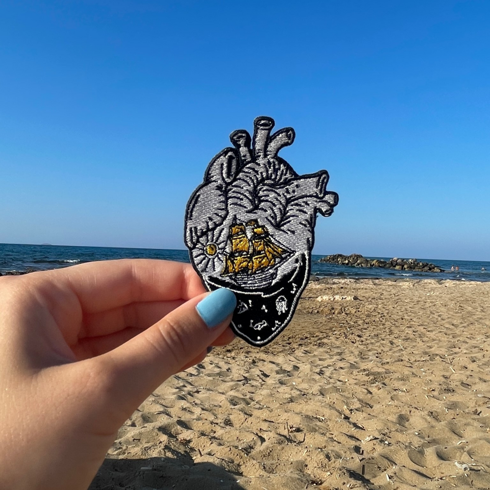 Meerliebhaber Patch in einer Frauenhand mit einem Strand im Hintergrund