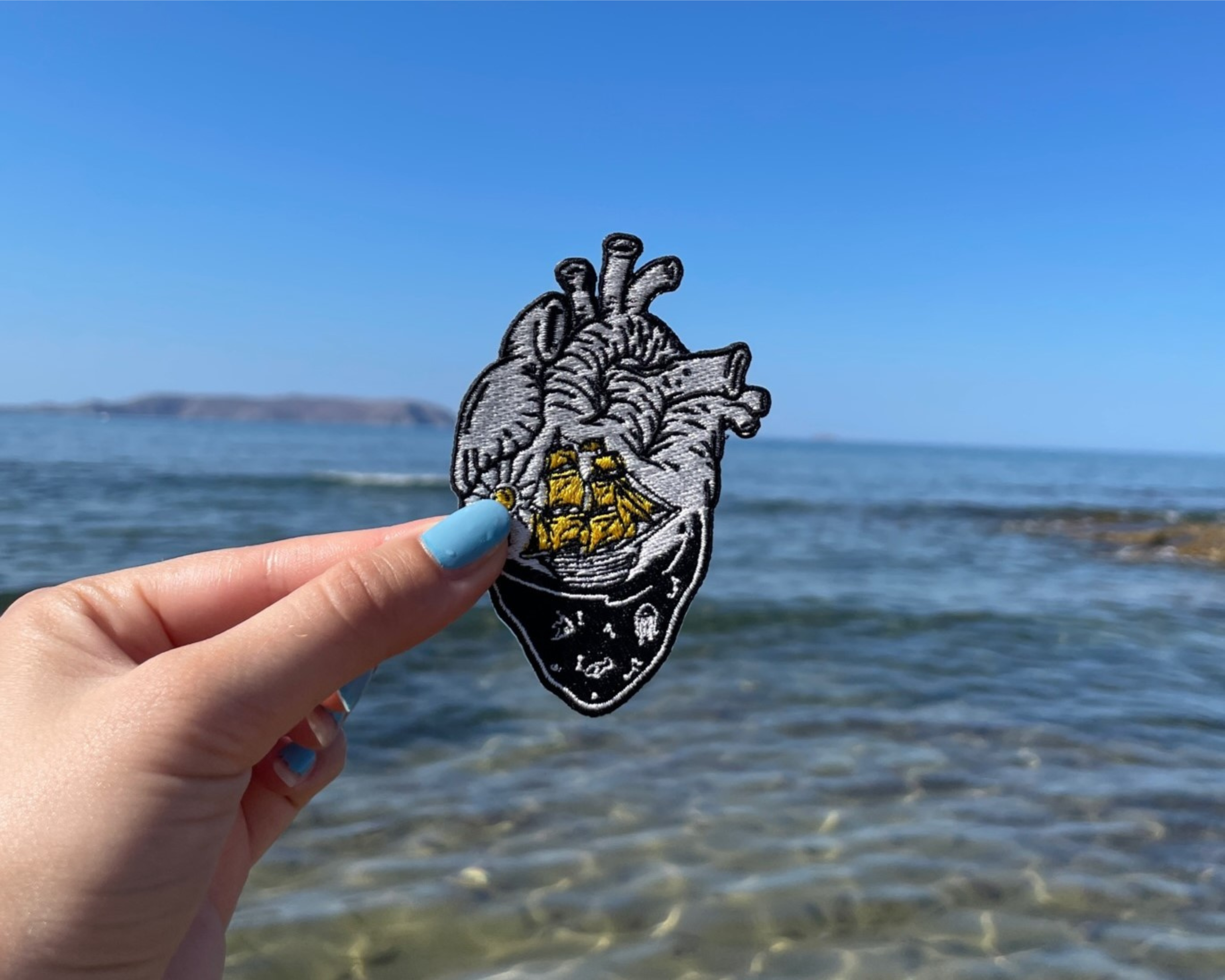 Meerliebhaber Patch in einer Frauenhand mit dem Meer im Hintergrund