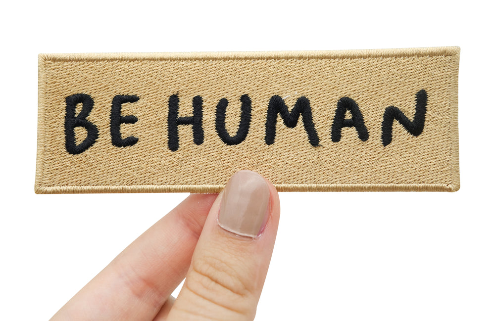 Frauenhand hält ockerfarbenen Be Human Patch