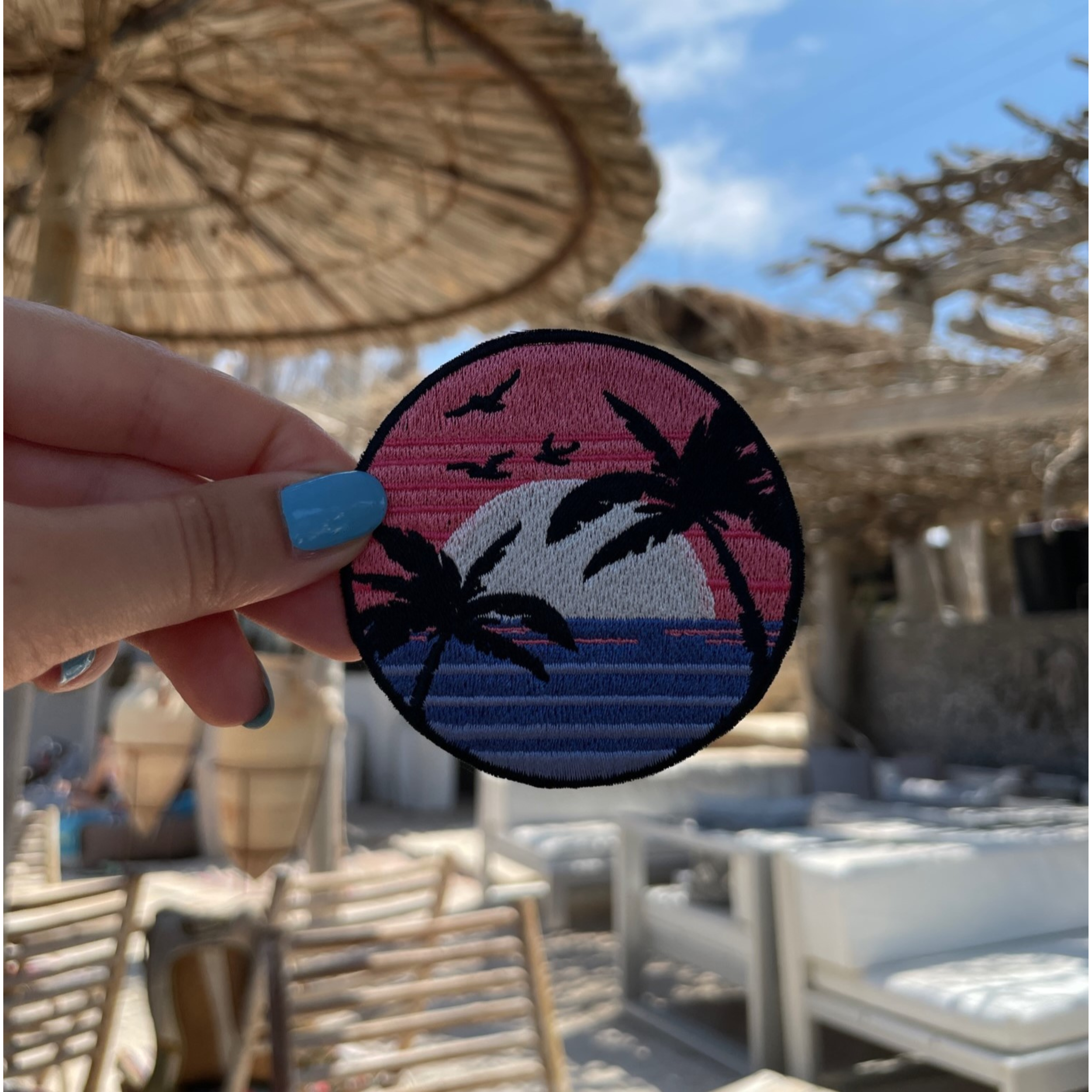 Sonnenuntergang Patch mit einer Strandbar im Hintergrund gehalten von einer Frauenhand
