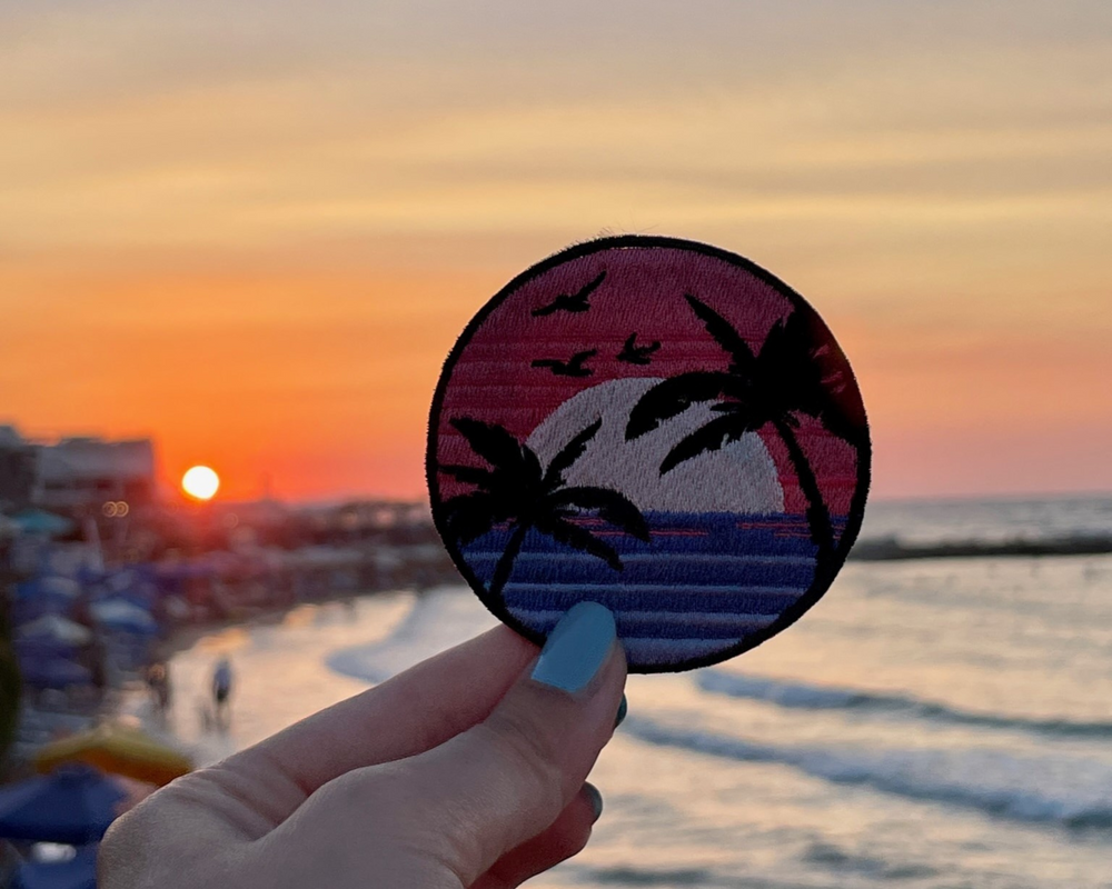Sonnenuntergang Patch mit dem Meer im Hintergund gehalten von einer Frauenhand