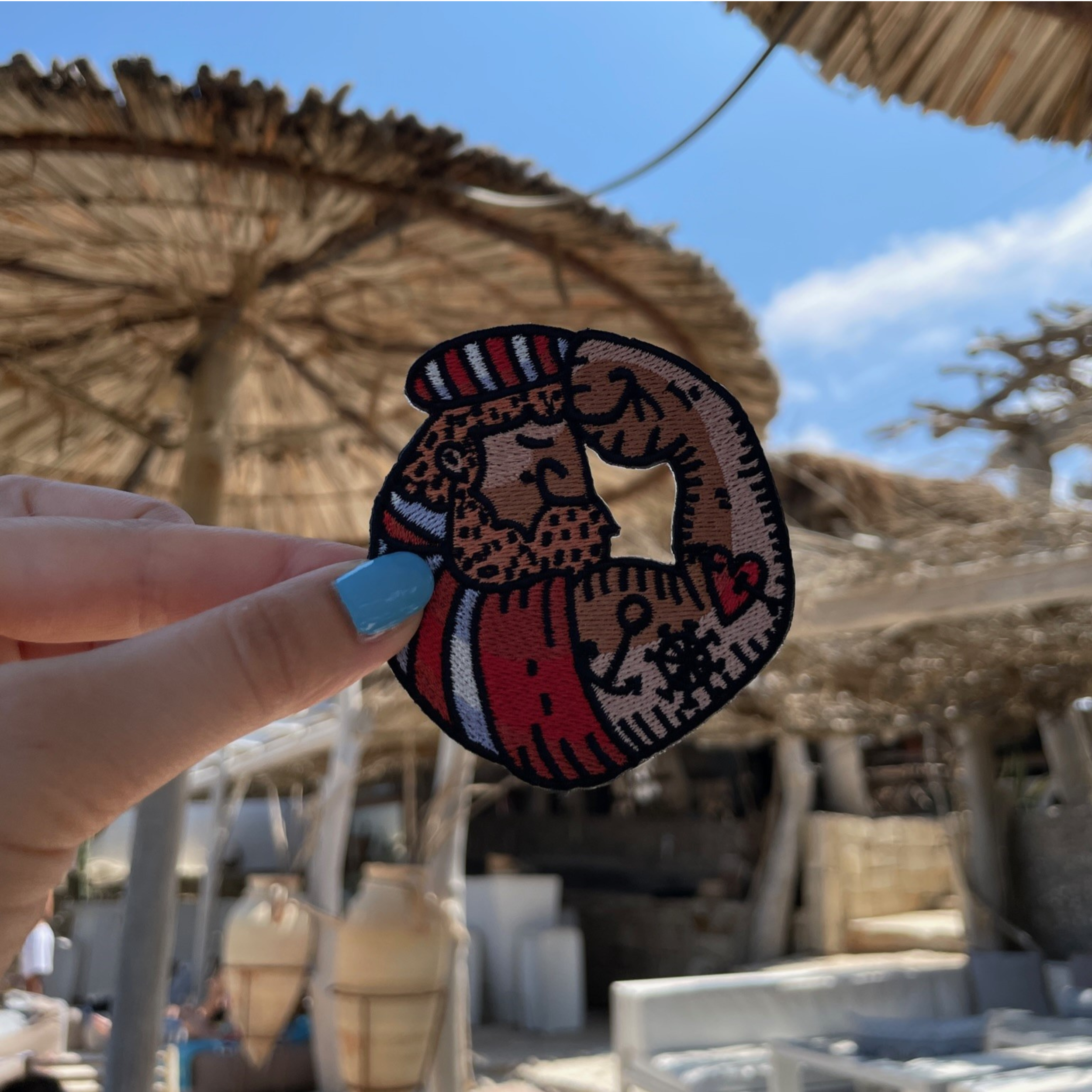 Seemann Patch gehalten von einer Frauenhand mit einer Strandbar im Hintergrund