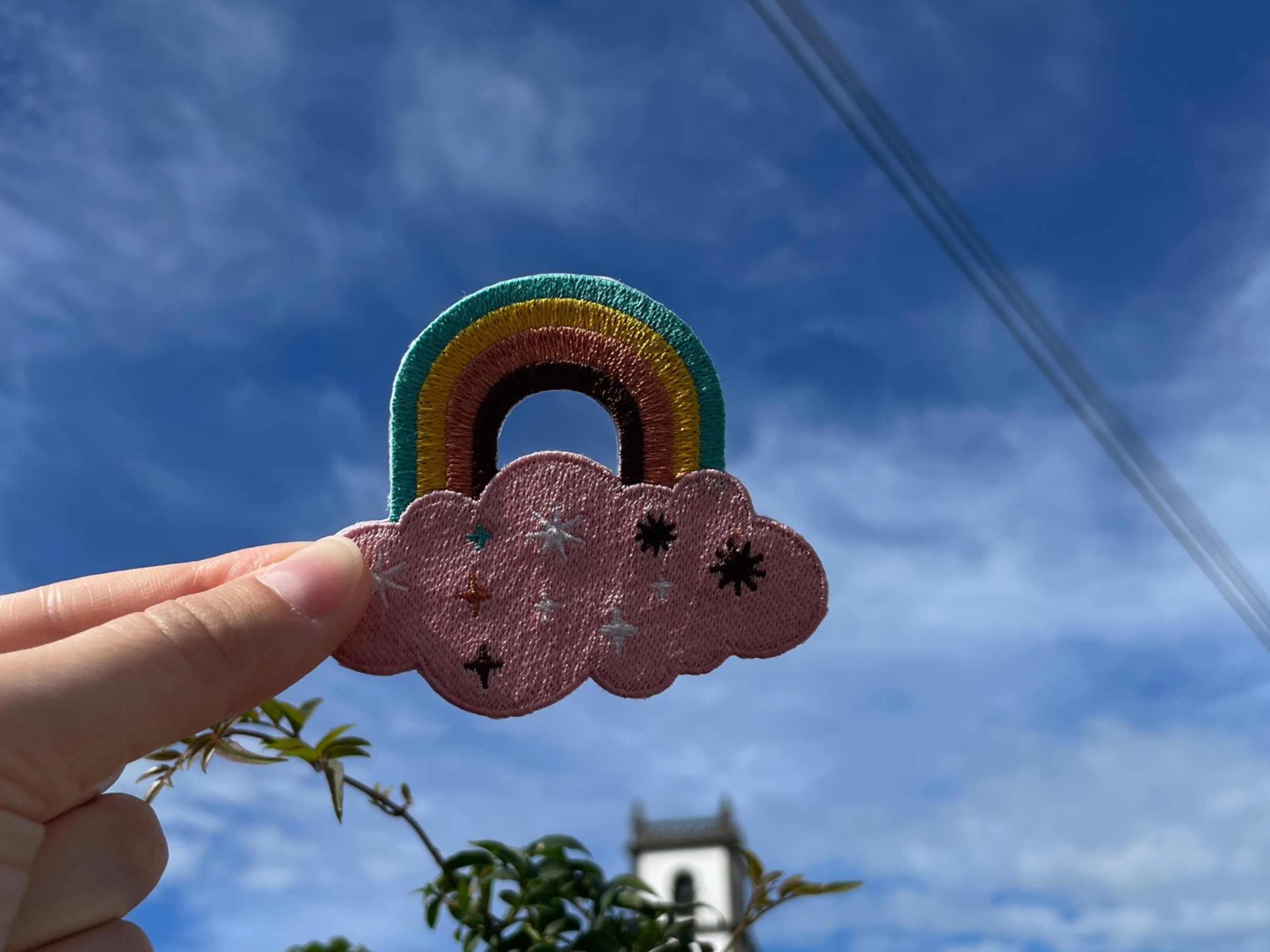 Regenbogen Patch gehalten von einer Frauenhand mit blauem Himmel im Hintergund