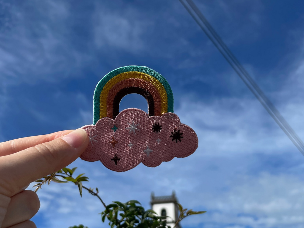 Regenbogen Patch gehalten von einer Frauenhand mit blauem Himmel im Hintergund