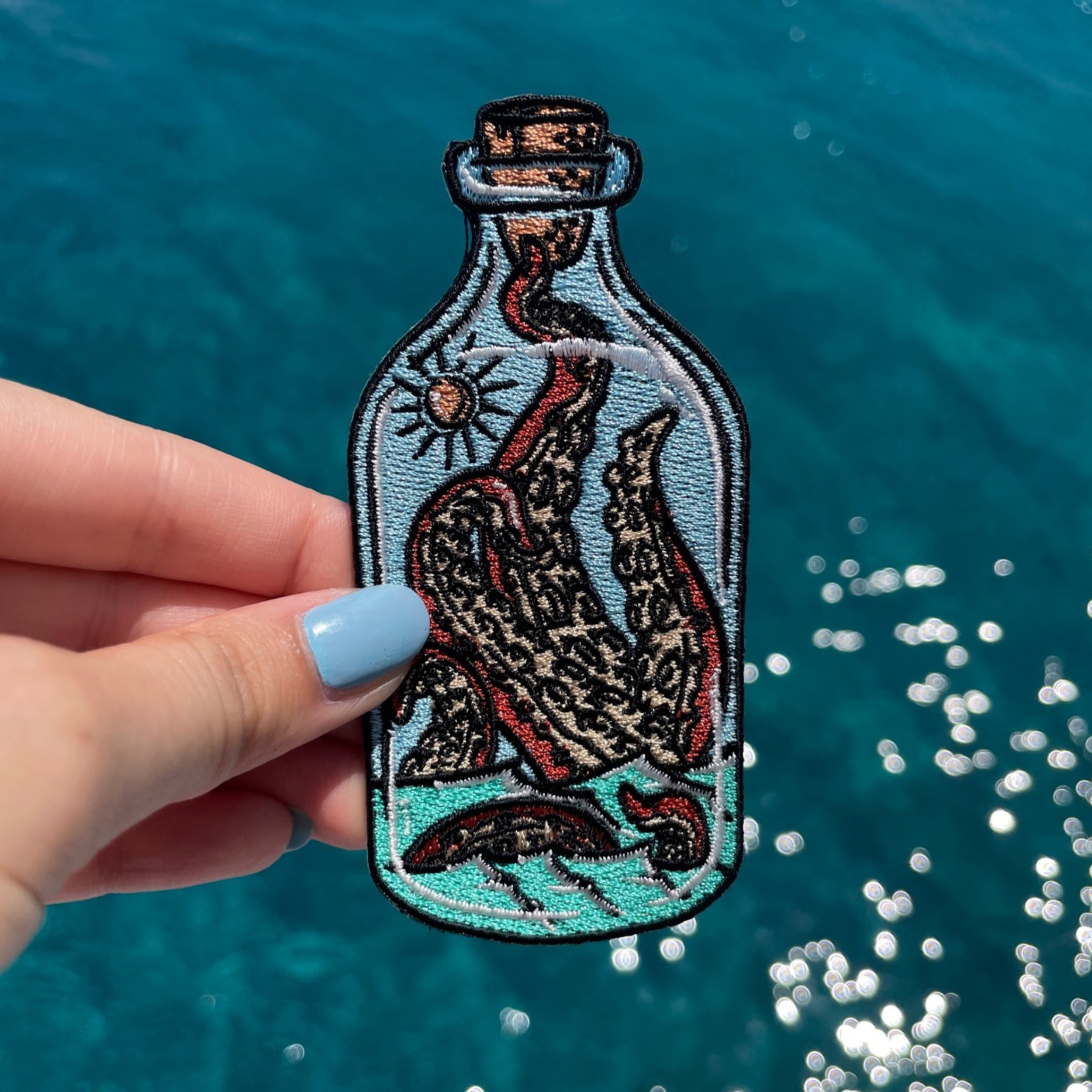 Krake in der Flasche Patch gehalten von einer Frauenhand mit dem Meer im Hintergund