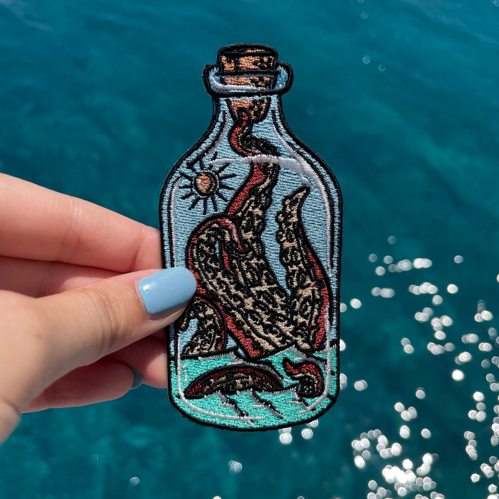 Krake in der Flasche Patch gehalten von einer Frauenhand mit dem Meer im Hintergund