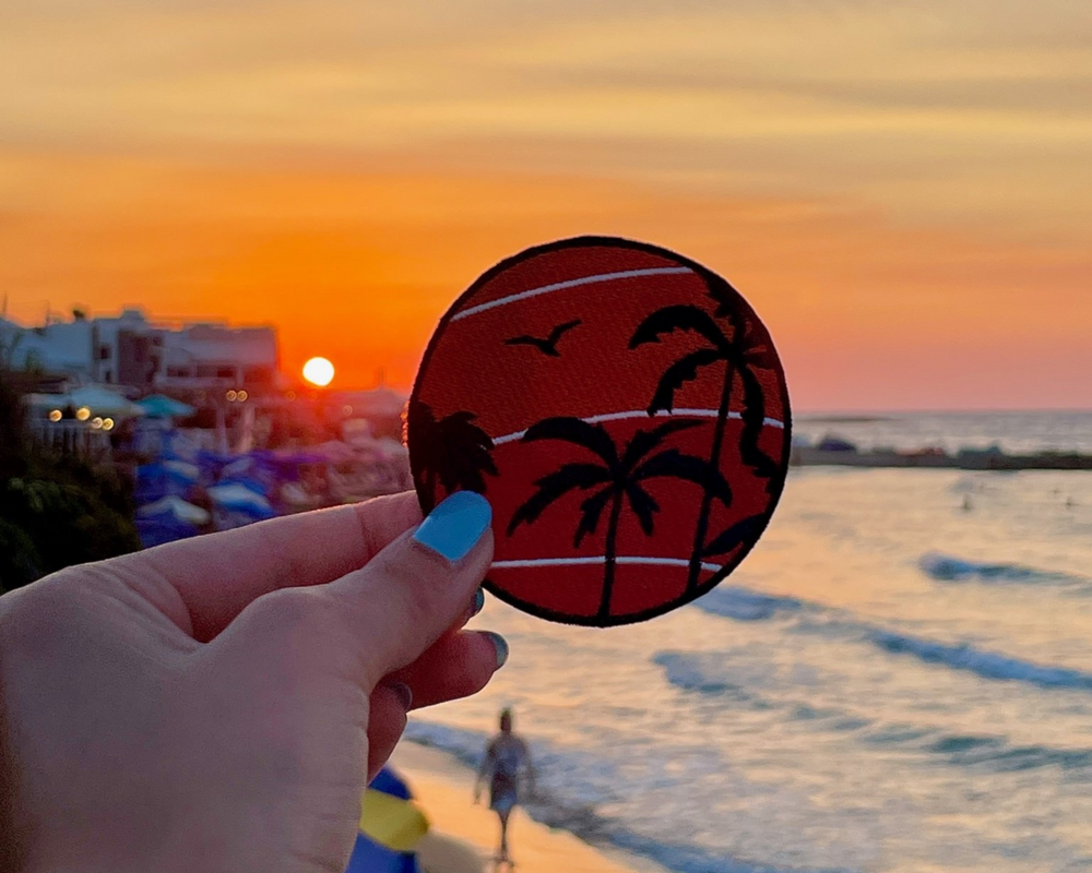 Sonnenuntergang Patch gehalten von einer Frauenhand mit einem Strand im Hintergrund