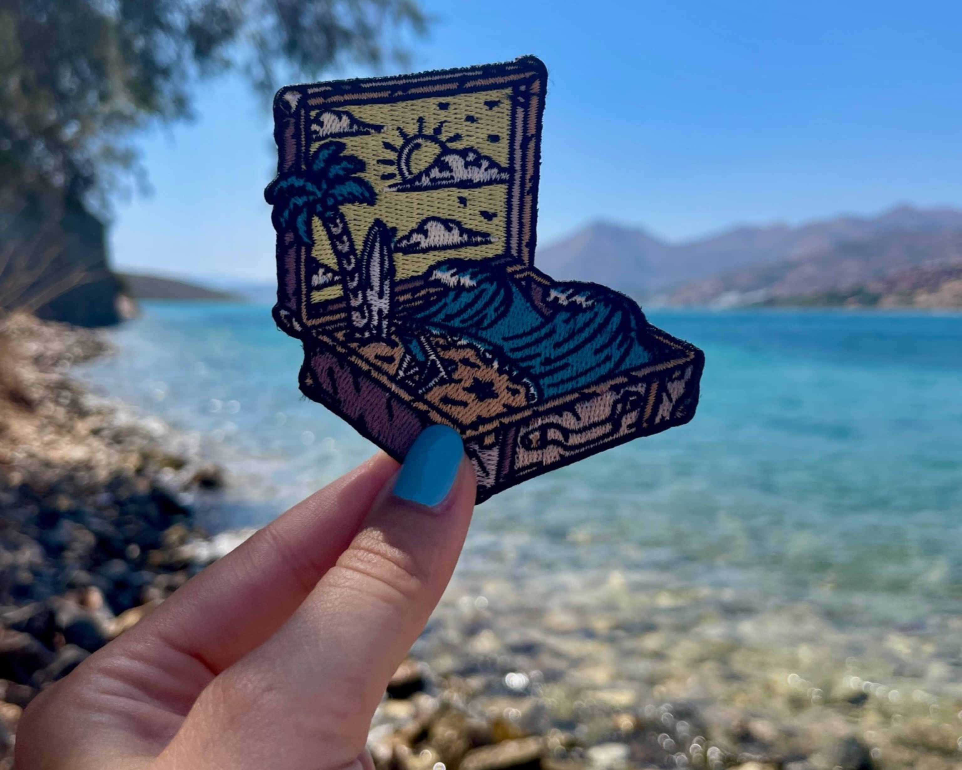 Strand im Koffer Patch gehalten von einer Frauenhand mit dem Meer im Hintergrund