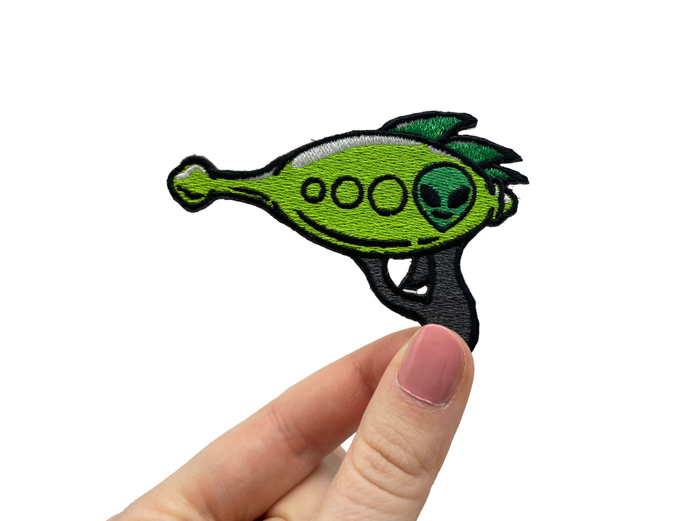 Frauenhand hält den Alien Pistole Patch