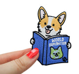 Frauenhand hält den World Domination Hund Patch