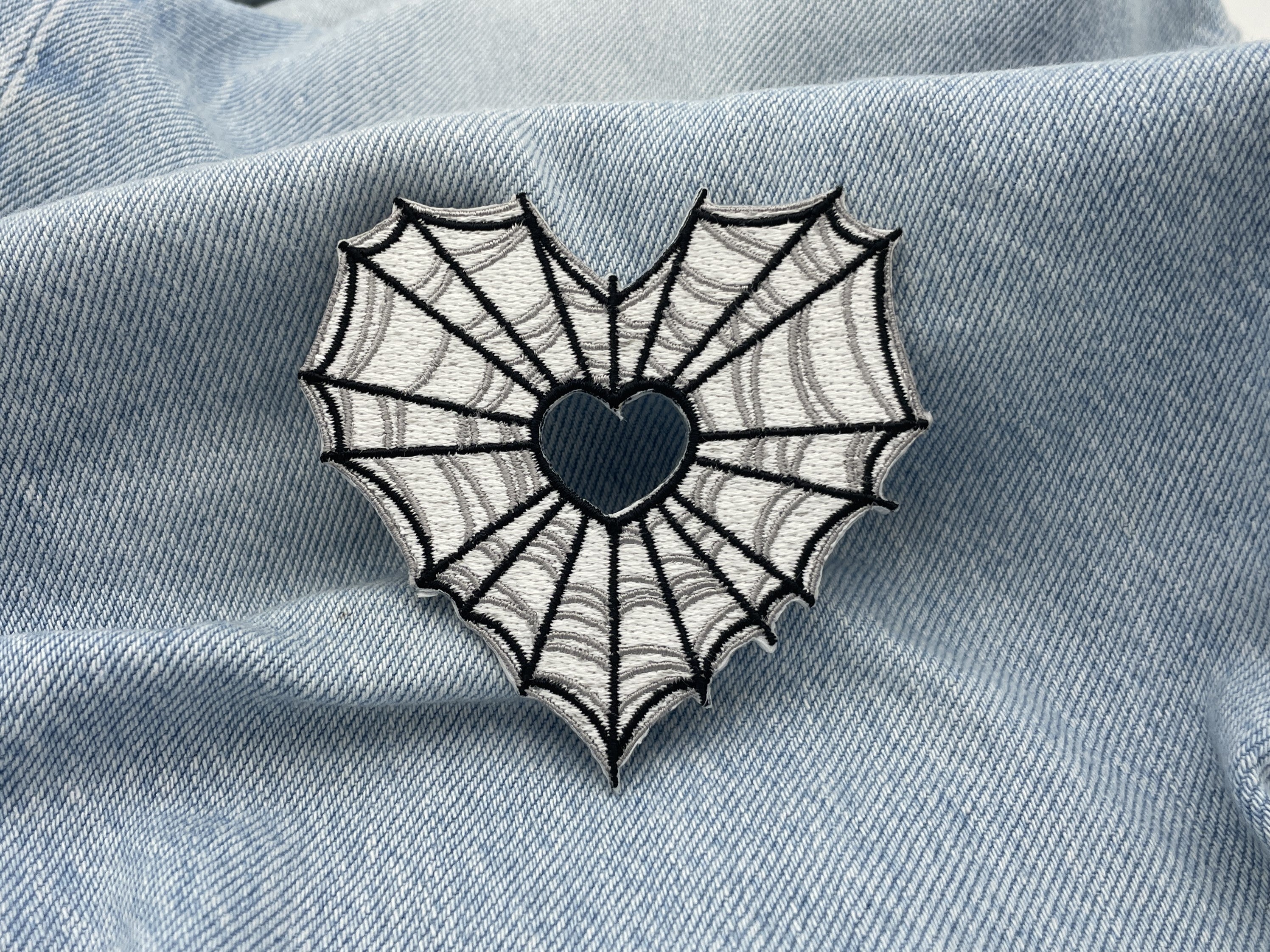 Spinnenweben Herz Patch auf hellblauer Jeans