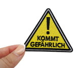 Frauenhand hält den Kommt Gefährlich Patch